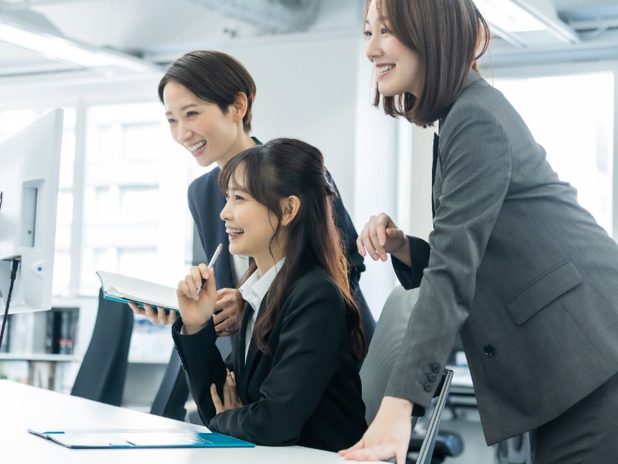 オフィスで社会人と一緒に画面を見ながら実務に取り組む学生